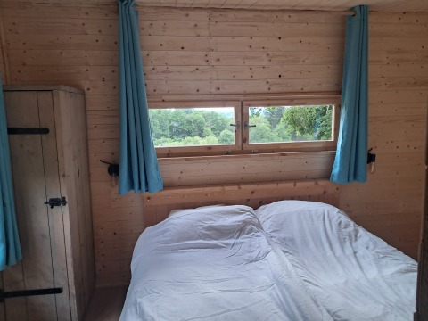 Interieur van een houten lodge met blauwe gordijnen, raam en tweepersoonsbed op Camping Junora, Avignon.