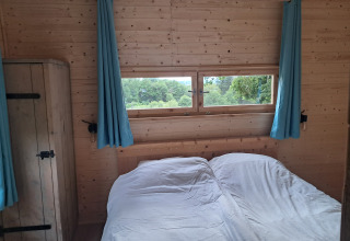 Interieur van een houten lodge met blauwe gordijnen, raam en tweepersoonsbed op Camping Junora, Avignon.