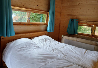 Slaapkamer in lodge Avignon op Camping Junora in Frankrijk, houten muren, tweepersoonsbed en blauwe gordijnen.