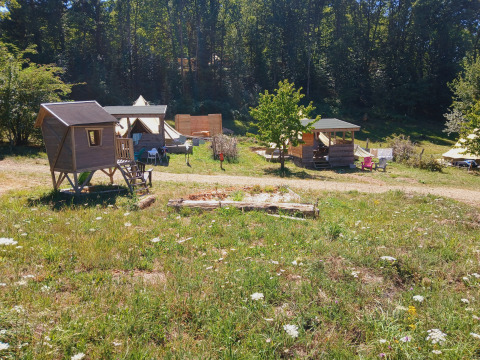 Photo of a lodge campground with wooden cabins, tents and outdoor seating surrounded by greenery and woods.
