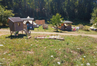 Photo of a lodge campground with wooden cabins, tents and outdoor seating surrounded by greenery and woods.