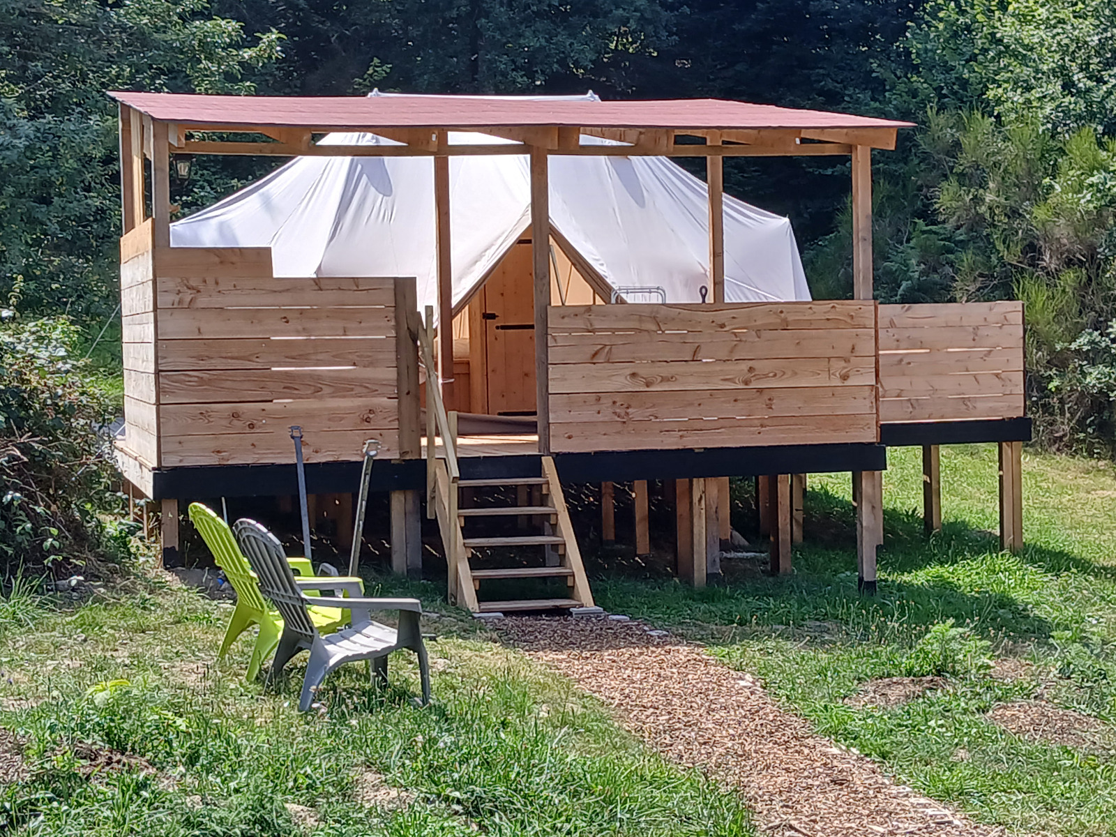 Emperor Bell Tent lodge met verhoogd houten terras, tentstructuur en buitenstoelen in groene omgeving.