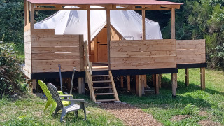 Emperor Bell Tent lodge featuring elevated wooden deck, tent structure, and outdoor chairs in greenery.
