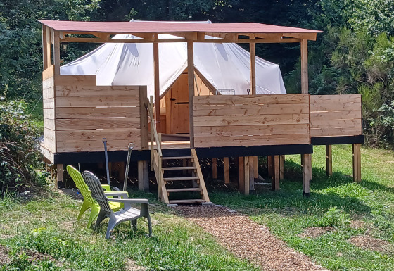 Emperor Bell Tent lodge con terrazza in legno rialzata, struttura a tenda e sedie all'aperto tra il verde.