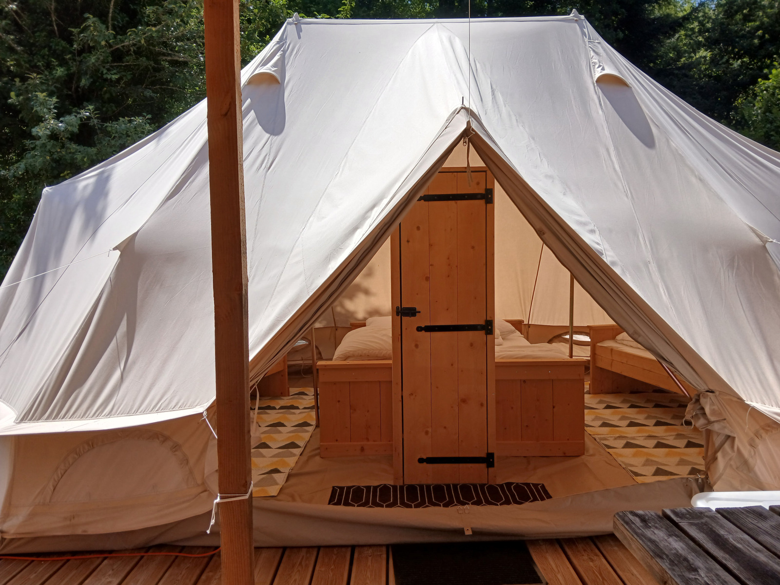 Ingang van de luxe Emperor Bell Tent op Camping Junora in Frankrijk, met houten meubels binnenin.
