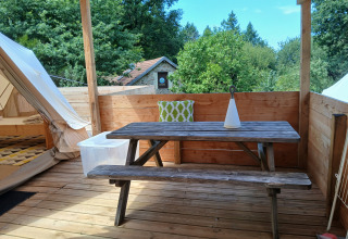 Terrazza esterna presso Emperor Bell Tent al Campeggio Junora in Francia, con tavolo di legno e cuscino verde.