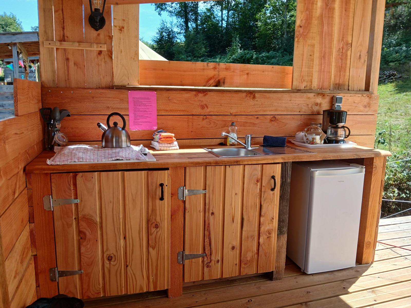 Buiten keuken van hout met gootsteen, waterkoker en koelkast bij Emperor Bell Tent op Camping Junora, Frankrijk.