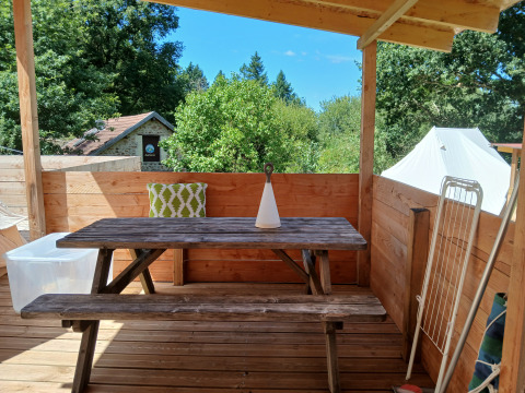 Houten terras met bank, tafel en kussen bij Emperor Bell Tent, Camping Junora in Frankrijk, omgeven door bomen.