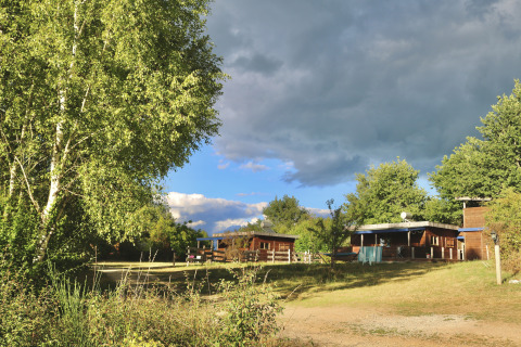 Area verde con alberi e chalet in legno presso Eco-Chalet EXTRA al Campeggio Junora, Francia.