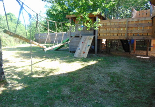 Buitenspeeltuin met boomhut, touwbrug en klimwand bij Eco-Chalet EXTRA op Camping Junora in Frankrijk.