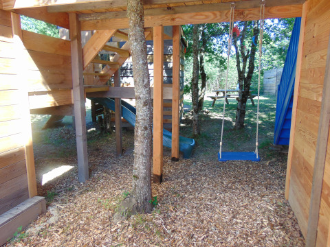 Boomhut met schommel, glijbaan en picknicktafel bij Camping Junora in Frankrijk, omringd door natuur.