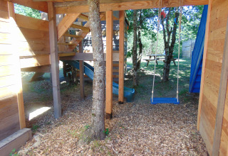 Boomhut met schommel, glijbaan en picknicktafel bij Camping Junora in Frankrijk, omringd door natuur.