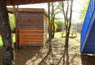Foto van de Eco-Chalet EXTRA boomhut op Camping Junora in Frankrijk, met tafels en bomen.