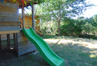 Boomhut met groene glijbaan en gekleurde vlaggetjes bij Eco-Chalet EXTRA, Camping Junora, Frankrijk.