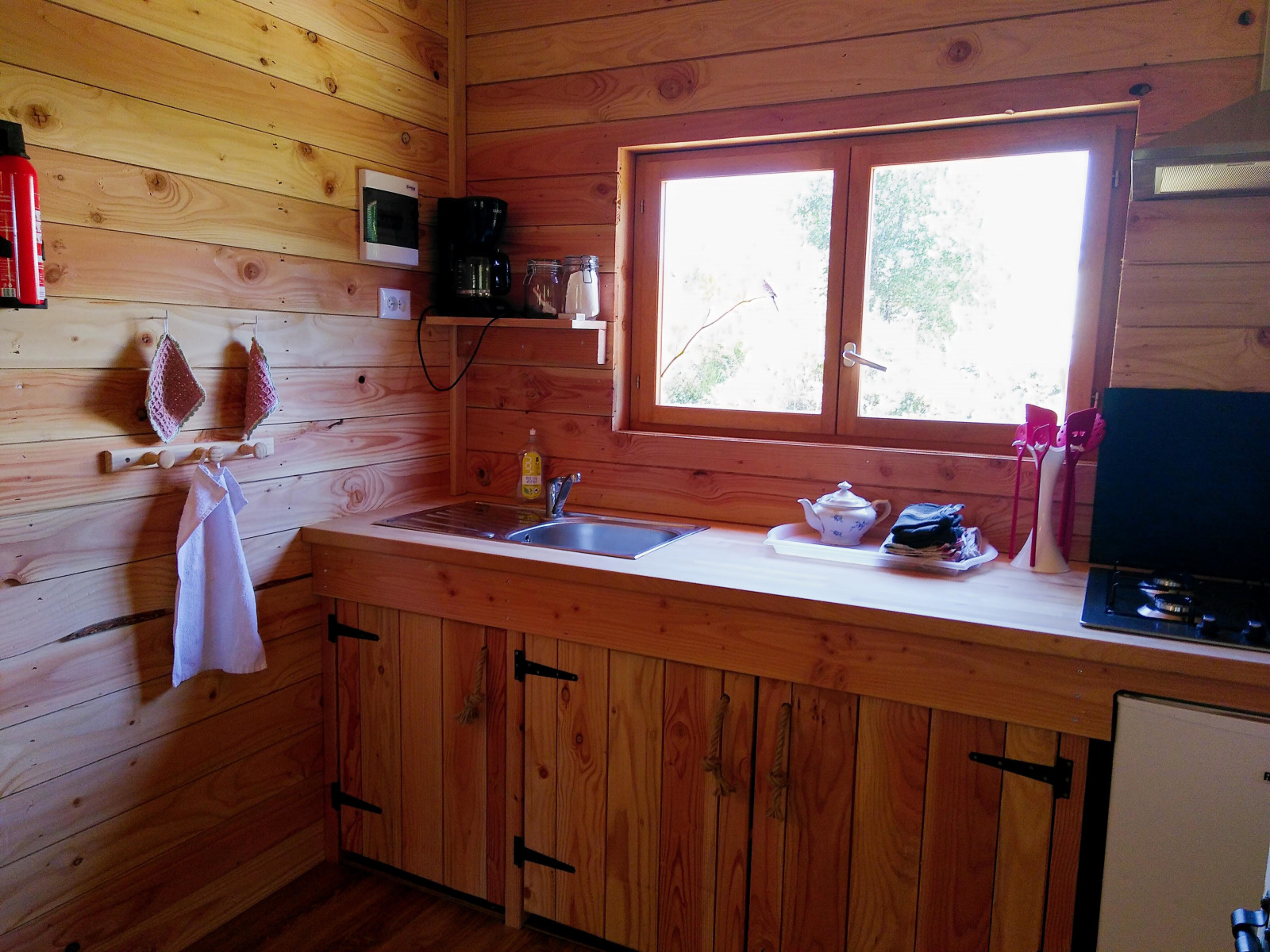 Knusse houten keuken in Eco-Chalet EXTRA op Campsite Junora, Frankrijk, met gootsteen, fornuis en raam.
