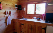 Cozy wooden kitchen in Eco-Chalet EXTRA at Campsite Junora, France, with sink, stove, and window view.