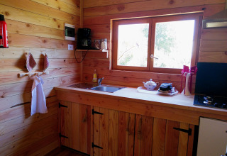 Accogliente cucina in legno dell’Eco-Chalet EXTRA al campeggio Junora, con lavello e fornello.