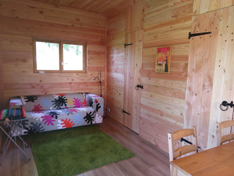 Interieur van Eco-Chalet EXTRA boomhut op Camping Junora in Frankrijk met houten wanden en kleurrige bank.