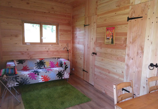 Interieur van Eco-Chalet EXTRA boomhut op Camping Junora in Frankrijk met houten wanden en kleurrige bank.