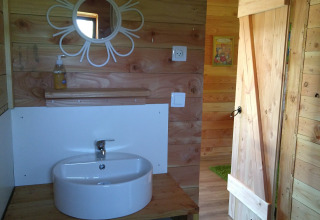 Houten badkamer met rond bloemenspiegel, wasbak en handdoeken in Eco-Chalet EXTRA, Camping Junora, Frankrijk.