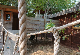 Boomhut bij Eco-Chalet EXTRA op Camping Junora in Frankrijk, met touwen en houten speelstructuur.