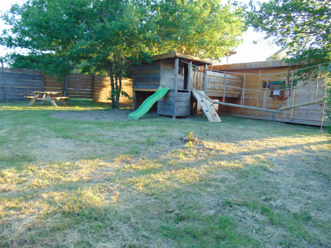 Eco-Chalet EXTRA boomhut en speeltuin bij Camping Junora in Frankrijk, omgeven door gras en bomen.