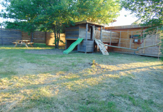 Eco-Chalet EXTRA boomhut en speeltuin bij Camping Junora in Frankrijk, omgeven door gras en bomen.
