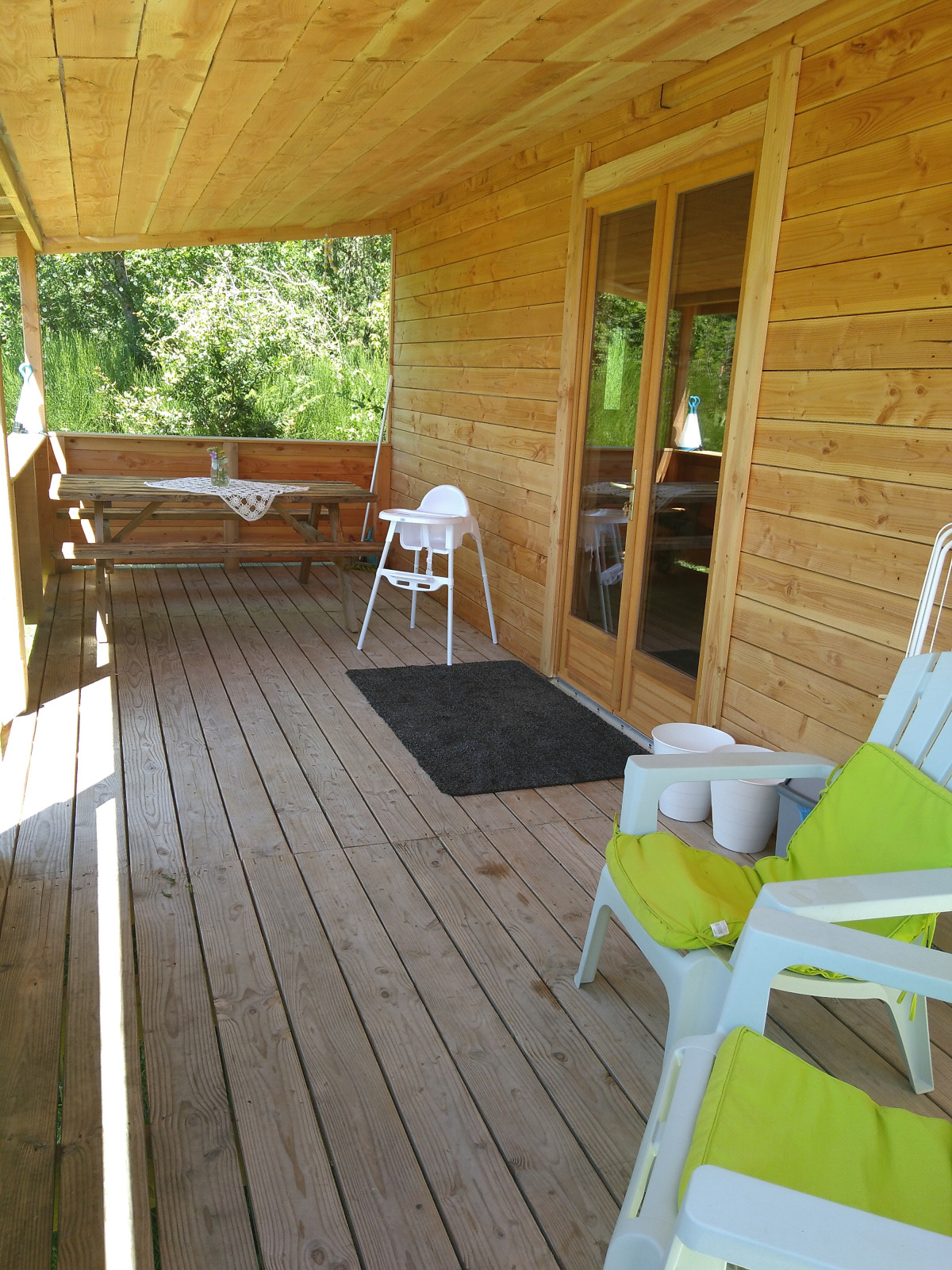 Houten veranda bij Eco-Chalet EXTRA, Camping Junora, Frankrijk, met stoelen, tafel en uitzicht op groen.