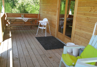 Houten veranda bij Eco-Chalet EXTRA, Camping Junora, Frankrijk, met stoelen, tafel en uitzicht op groen.