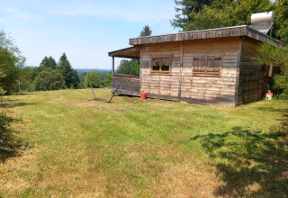 Holzchalet mit Solarpanel auf dem Dach, umgeben von Wiese und Wald auf dem Campingplatz Junora, Frankreich.