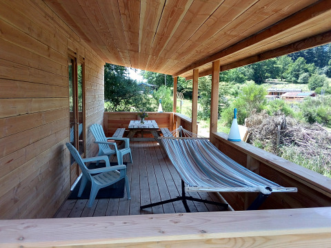Veranda in legno con amaca, sedie e tavolo da picnic all’eco-chalet di lusso presso il campeggio Junora, Francia.