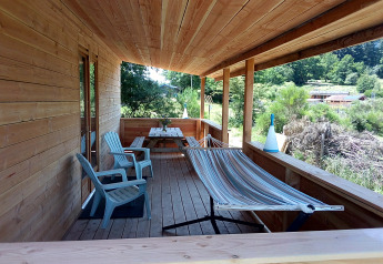 Træveranda med hængekøje, stole og picnicbord på luksus øko-chalet på Campingplads Junora i Frankrig.