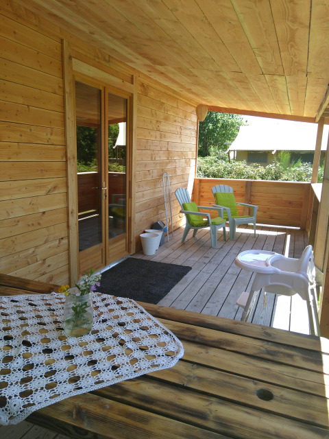 Veranda in legno dello chalet 'Self-sufficient, luxury eco-chalet' al Campeggio Junora con sedie e fiori, Francia.