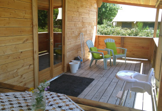 Holzveranda am 'Self-sufficient, luxury eco-chalet' auf dem Campingplatz Junora mit Stühlen und Blumen, Frankreich.