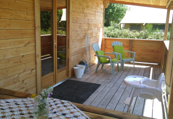 Veranda in legno dello chalet 'Self-sufficient, luxury eco-chalet' al Campeggio Junora con sedie e fiori, Francia.