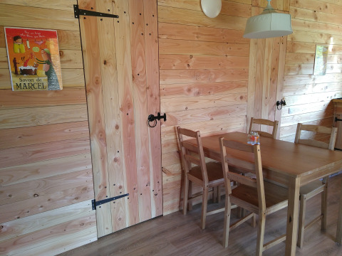Salle à manger en bois avec affiches, quatre chaises, table et suspension dans un éco-chalet luxueux et autonome.
