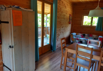 Vista interior de un acogedor chalet de madera con mesa de comedor, sofá colorido y terraza visible por puertas de vidrio.