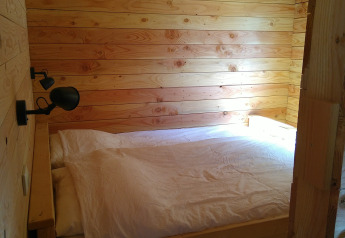 Bedroom with wooden walls and double bed in the Self-sufficient, luxury eco-chalet at Campsite Junora, France.