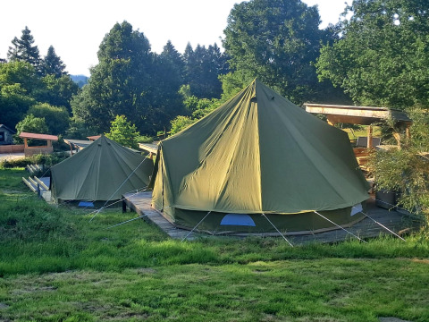 Two bell tents on a wooden platform at Bell tent 6M lodge, surrounded by lush greenery and tall trees.
