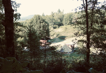 Vue sur une tente dans une clairière entourée d’arbres au Bell tent «6M», Campsite Junora en France.