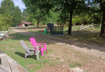 Espace extérieur près de la tente Bell «6M» au Camping Junora, avec fauteuils, arbres et aire de jeux.