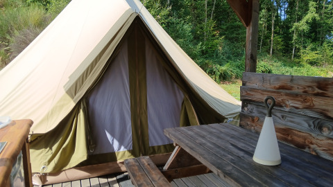 Bell tent «6M» at Campsite Junora in France, showing a wooden picnic table and forest backdrop.