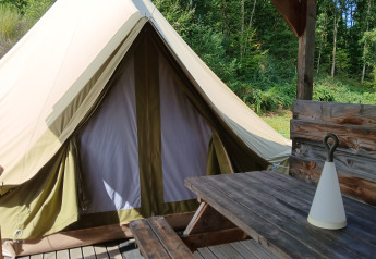 Bell Tent «6M» am Campsite Junora in Frankreich, mit Holztisch und grüner Waldlandschaft.