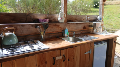 Outdoor kitchen at Bell tent “6M” at Campsite Junora in France, featuring a stove, sink, and utensils.
