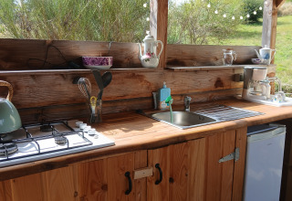Outdoor kitchen at Bell tent “6M” at Campsite Junora in France, featuring a stove, sink, and utensils.