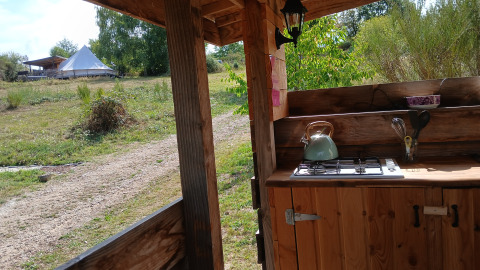 View from the outdoor kitchen at Bell tent «6M», Campsite Junora, France, showing the tent and greenery.