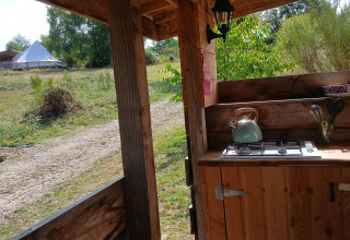 View from the outdoor kitchen at Bell tent «6M», Campsite Junora, France, showing the tent and greenery.