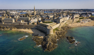 Vista aérea de la ciudad amurallada de Saint-Malo en Bretaña, Francia, con playas y murallas históricas.