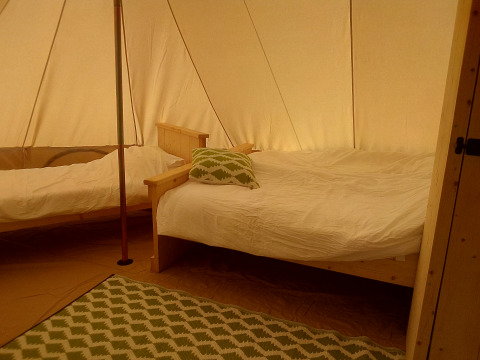 Interior of a Bell tent at Campsite Junora in France, featuring two wooden beds, white linens, and a green rug.
