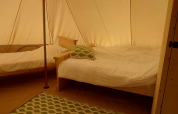 Indersiden af en Bell tent på Campsite Junora i Frankrig, med to træsenge og et grønt tæppe på gulvet.